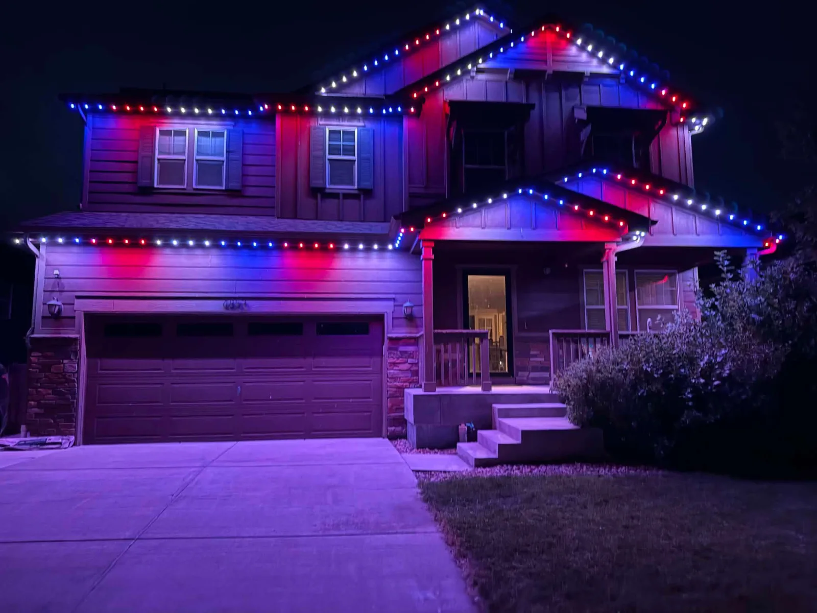 Two-story home displaying red, white, and blue permanent lighting for the Fourth of July