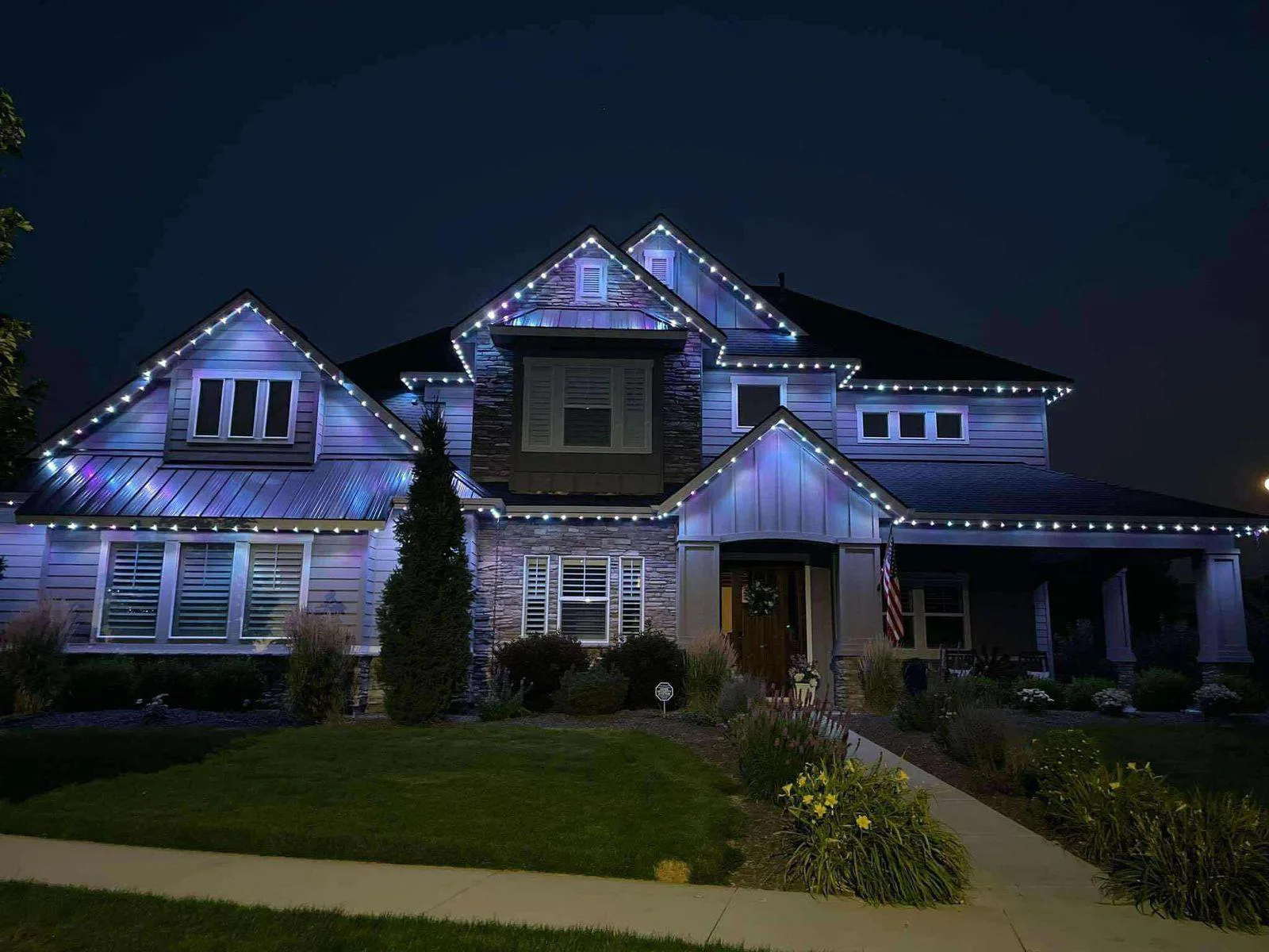 Craftsman home with multicolor permanent roofline lighting at night